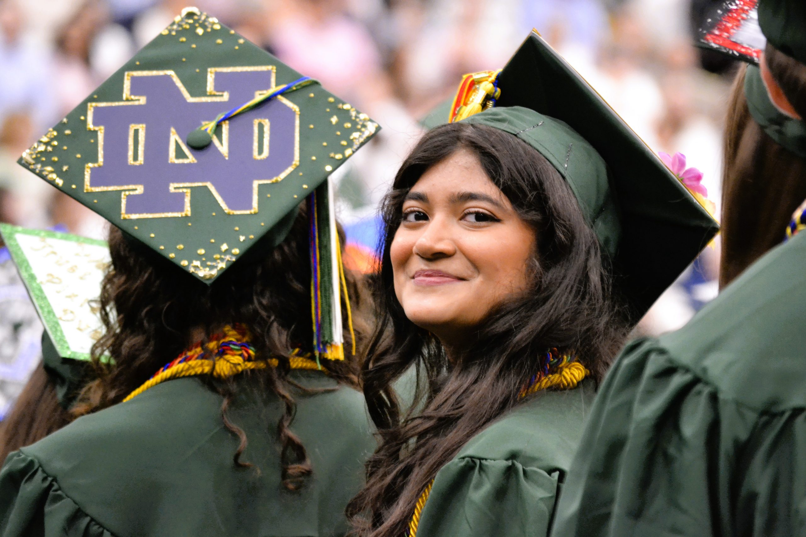 Senior in green cap and gown smiles at camera.