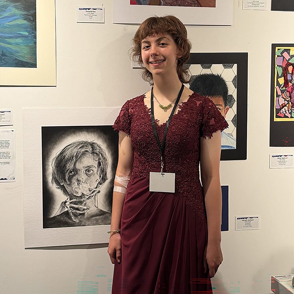 A student standing in front of a wall with artwork hanging on it