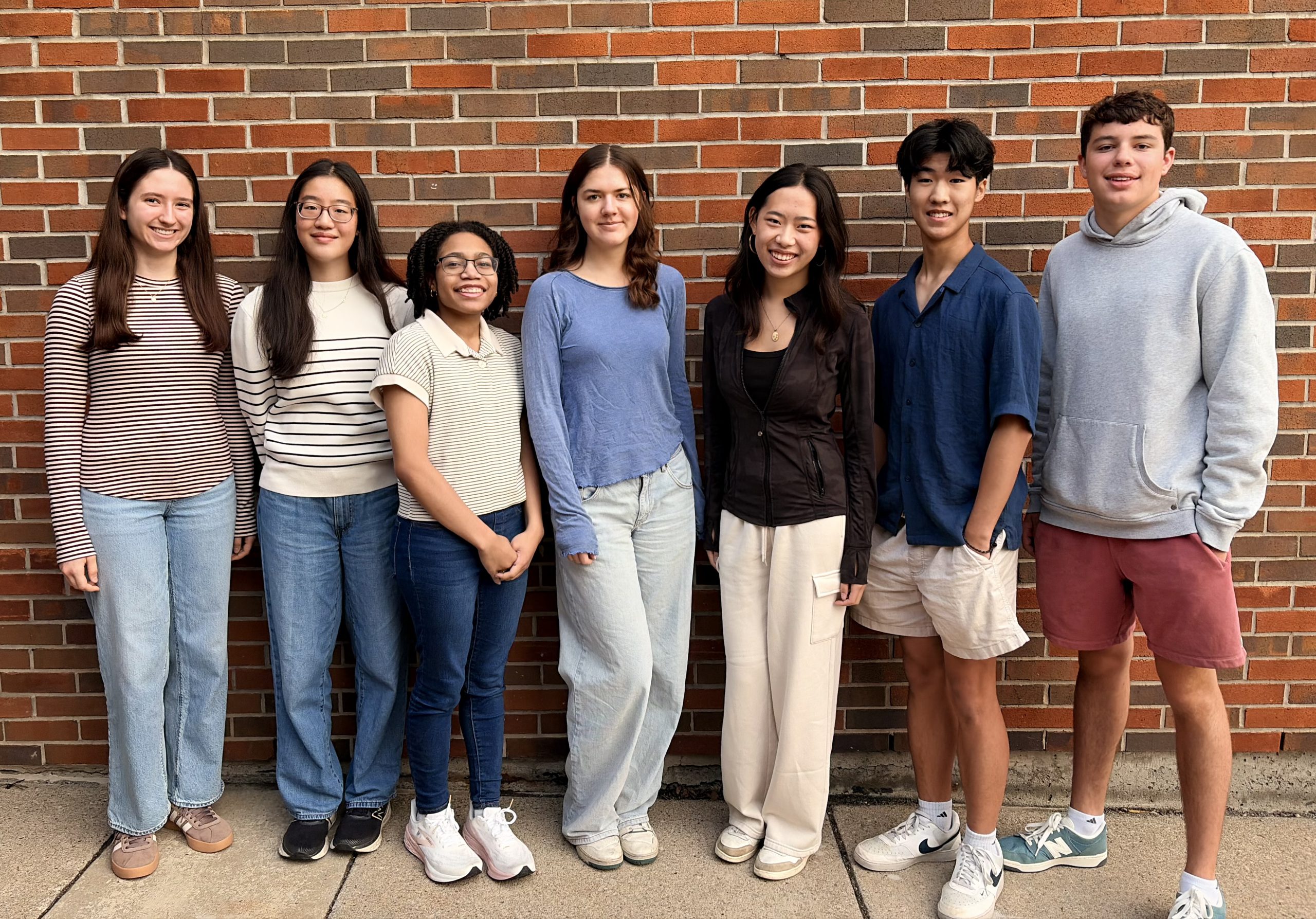 A group of students poses together in front of a brick wall.